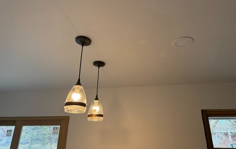 Two modern glass pendant lights hanging from a white ceiling alongside a recessed light fixture.