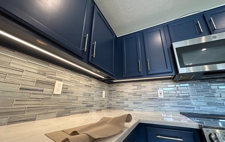 Modern kitchen with navy blue cabinets, white quartz countertops, and LED under cabinet lighting.