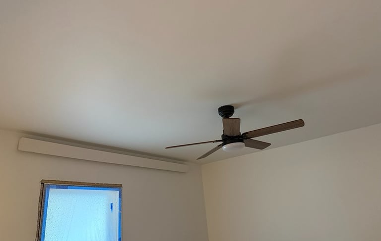 A modern dark wood ceiling fan with light installed on a white bedroom ceiling.