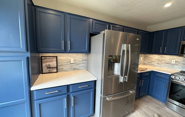 Modern kitchen with blue painted cabinets, white quartz countertops, and stainless steel appliances.