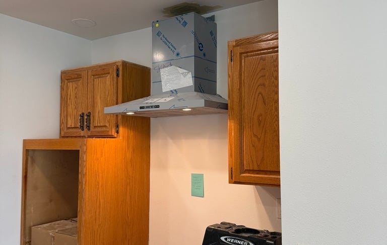A stainless steel range hood installation in a kitchen remodel with oak cabinets and a Werner stepladder.