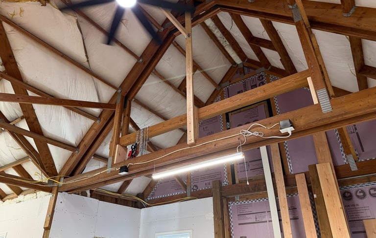 Vaulted ceiling under construction with exposed wood trusses, rigid foam insulation, and a ceiling fan.