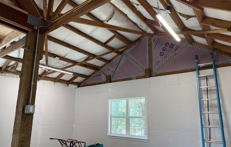 Garage workshop interior with white drywall, exposed wood ceiling trusses, and foam board insulation.