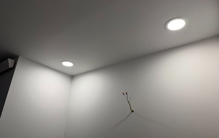 Modern recessed LED ceiling lights illuminating a white wall with exposed electrical wiring.