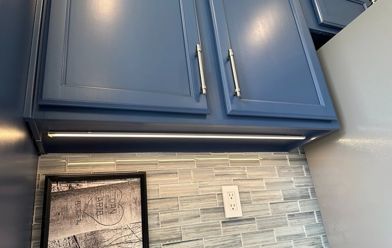Modern blue kitchen cabinets with LED under cabinet lighting and a gray glass tile backsplash.