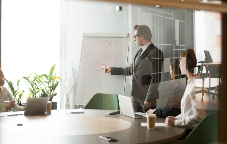 Professional businessman leading a corporate team meeting and pointing to a whiteboard diagram.