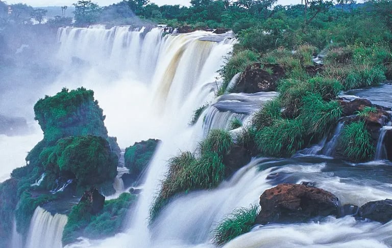 Panoramic view of Iguazu Falls with cascading water over green cliffs and lush rainforest landscape.