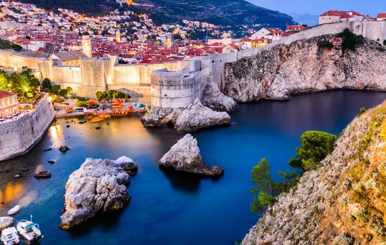 Night view of Dubrovnik Old Town walls and West Harbour with illuminated coastal fortifications in Croatia.
