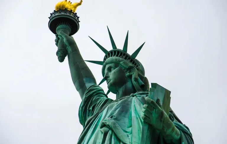 Low-angle view of the Statue of Liberty monument with its golden torch and crown against a grey sky.