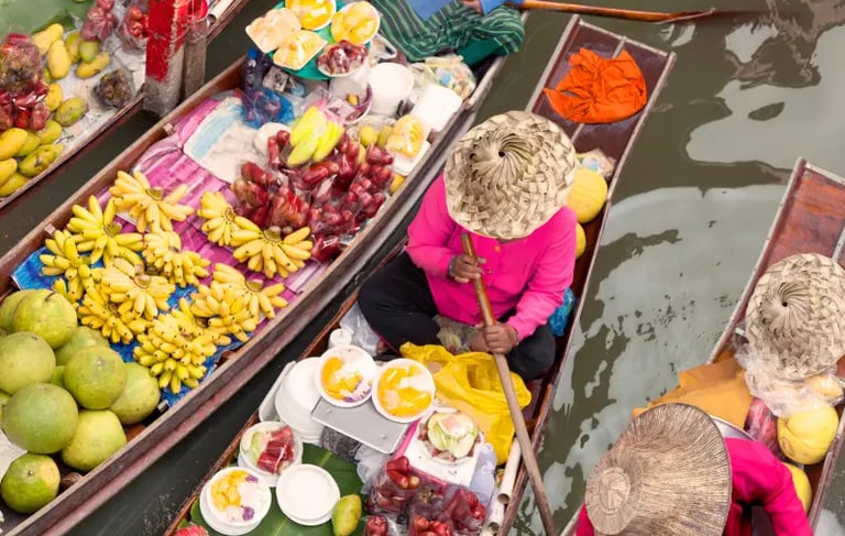 High angle view of vendors selling fresh tropical fruits from wooden boats at a Thai floating market.