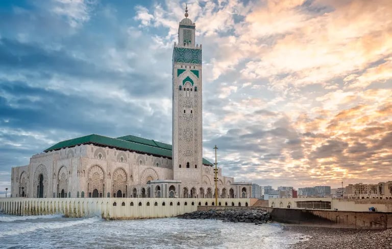 The Hassan II Mosque in Casablanca, Morocco, sits on the Atlantic coast under a sunset sky.