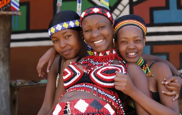 Three Ndebele women wearing traditional South African beaded jewelry and colorful headbands.