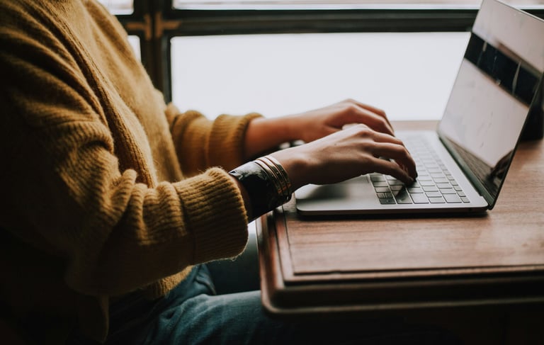 Photograph of a person sat at a desk with their hands on the keyboard of a laptop