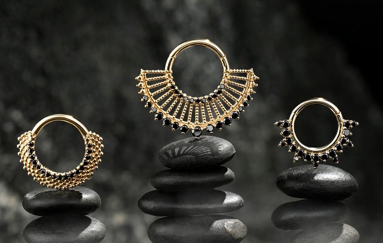 Three gold septum rings with black gemstone accents, displayed on stacked black stones against a dark background for e-com