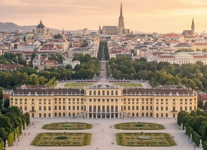 Aerial view of Schönbrunn Palace gardens and Vienna cityscape at golden hour