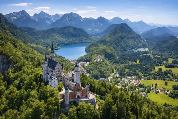 Aerial view of Neuschwanstein Castle surrounded by green Alps and lakes