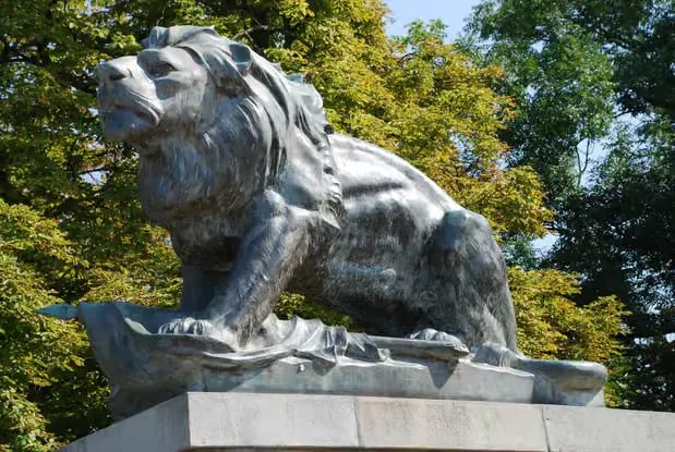 Bronze lion sculpture at Schlossberg Graz surrounded by green trees