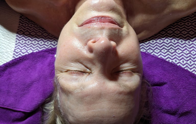 woman getting a facial with eyes closed on a purple towel