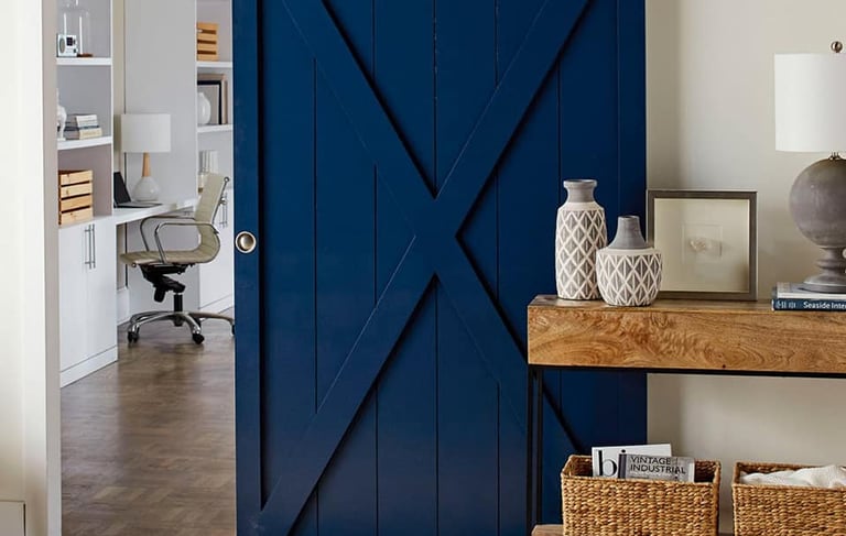 Modern navy blue sliding barn door with X-brace design leading to a home office.