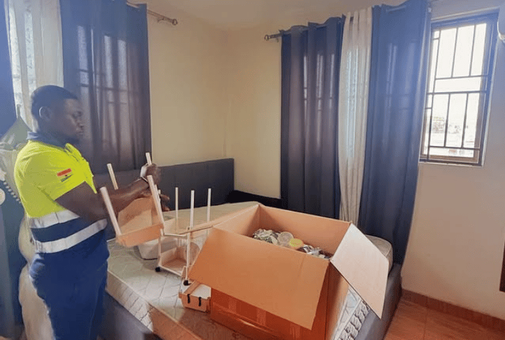 A professional mover in a yellow high-visibility vest with reflective strips and Ghanaian flag patch