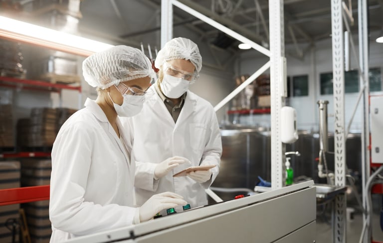 Two laboratory technicians wearing white coats and masks operating machinery in a food processing plant.