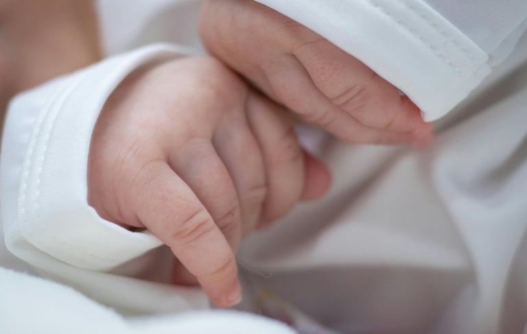 a baby's hand holding a finger on a white blanket
