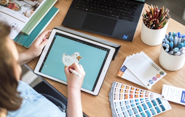 Arbeitsplatz mit Laptop, iPad, Farbkarten und Papierproben.