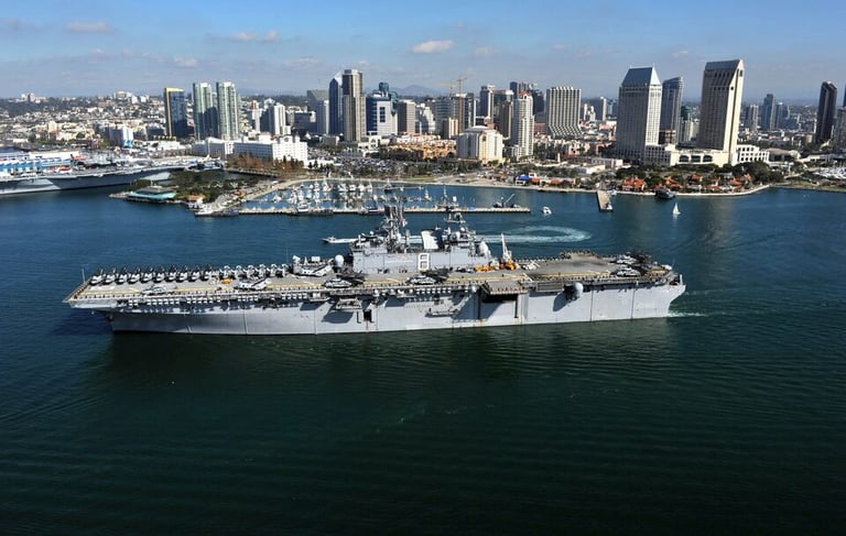a large Navy ship in the water with a city in the background
