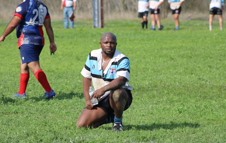 a black man in a striped shirt is kneeling down and holding a rugby ball