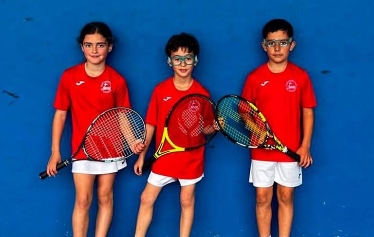 Niños y niñas de la escuela de frontón apoyados en la pared antes de jugar