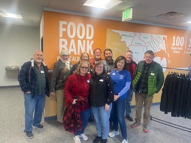 A group of people posing in front of the food back sign while volunteering to pack Christmas food