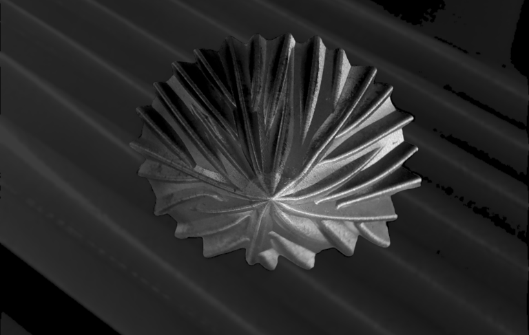 A decorative pleated metal bowl with a textured sunburst pattern on a dark ribbed surface.