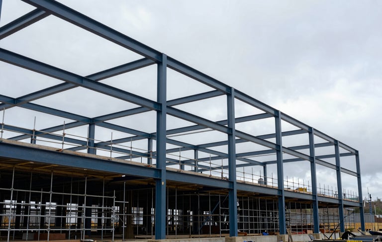 Clean, wide-angle architectural photography of a modern commercial construction site in Newcastle, Northern European / British setting. Features high-quality steel structure work and scaffolding against a bright, overcast sky. Professional, robust atmosphere with steel blue and dark charcoal tones.