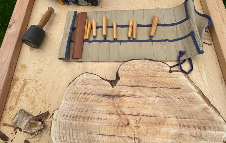 Large table with belt sander, wood knives, and live edge piece of wood