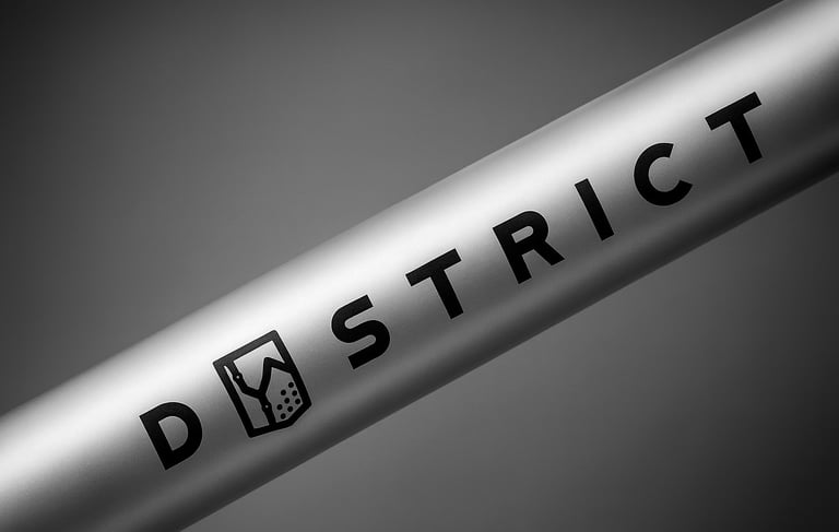 A close-up of a silver aluminum bike frame tube featuring the District brand logo in black text.