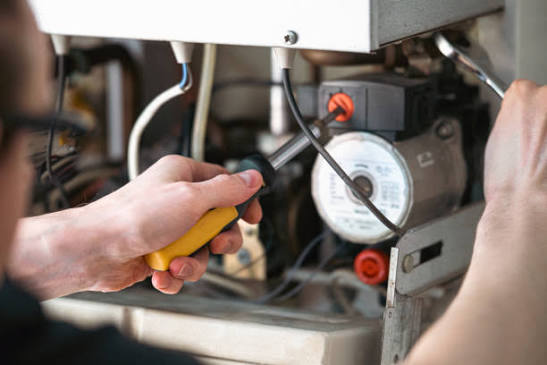 A technician using a screwdriver for professional boiler repair and heating system maintenance.