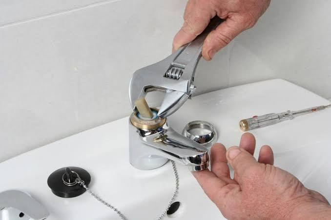 Plumber using an adjustable wrench to repair a leaking bathroom sink faucet.