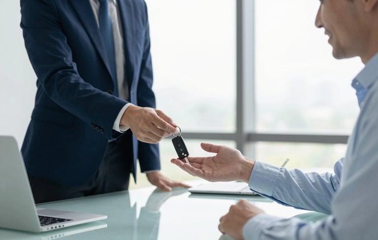 A high-resolution photography shot in a bright North American office. A professional person in a light blue shirt hands a set of car keys to a smiling client across a clean glass desk. The atmosphere is transparent and secure. Soft morning light streams through the window. The color palette emphasizes dark blue and off-white tones for a trustworthy financial service aesthetic.