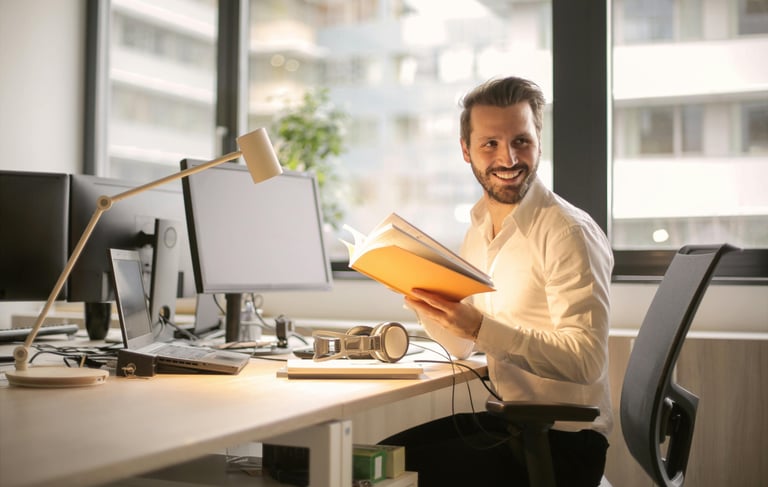 homme assis à un bureau et feuilletant un livre tourne la tête en souriant