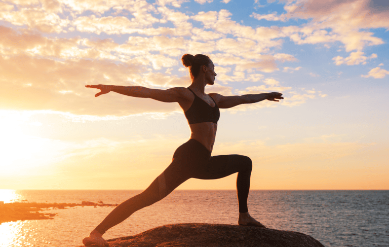 Woman yoga pose beside the ocean at sunset