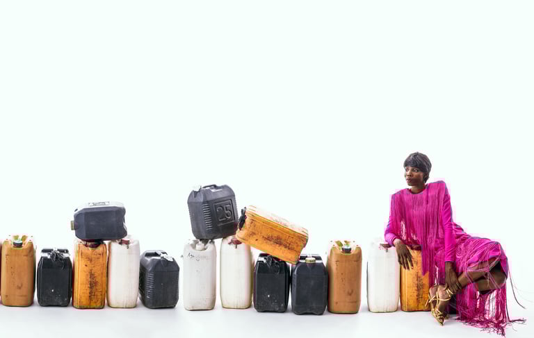 a woman in a pink dress sitting on a fuel keg at the end of a line of plastic fuel kegs