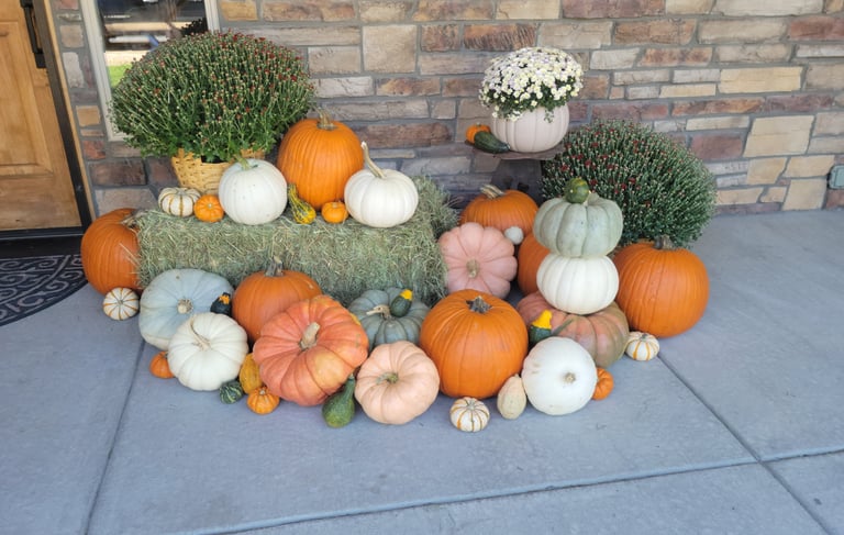 A pile of pumpkins and gourds with haybales and mum flowers on a porch