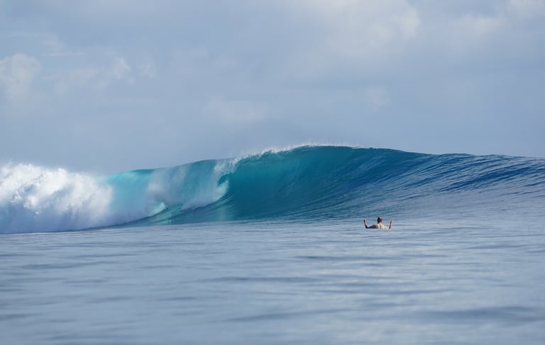 Crystal blue Mentawai wave breaking with surfer waiting in lineup
