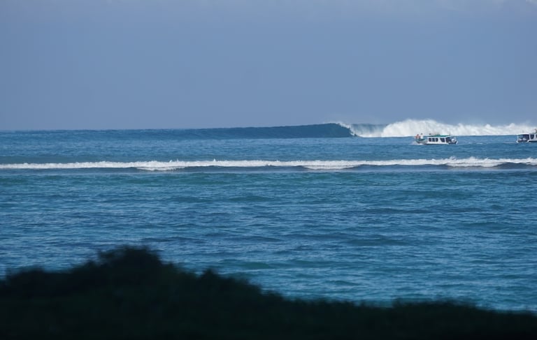 Breaking waves at Suicides surf spot near Toska with boats anchored in channel