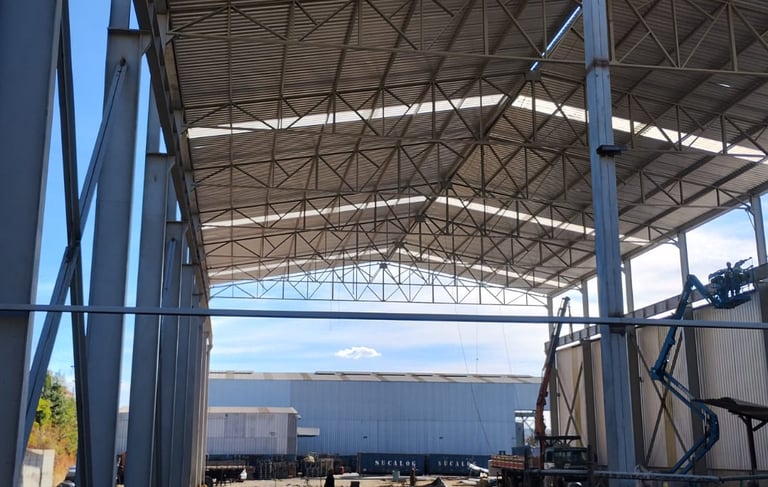 Estrutura metálica de galpão industrial em montagem, com cobertura treliçada e pilares aparentes.