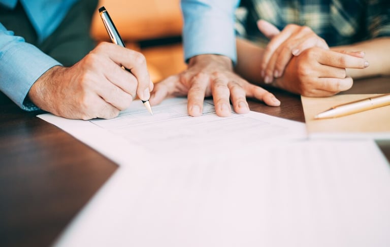 a man and woman sitting at a table with papers and pen