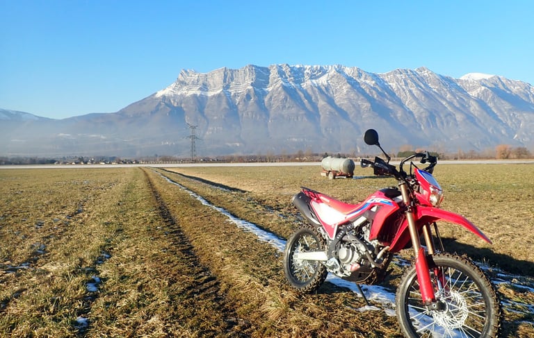 a red motorcycle parked in a field with mountains in the background