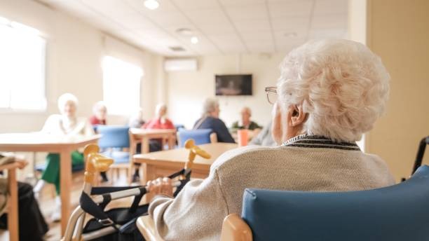 Una señora mayor está sentada a una mesa en un hogar de ancianos.