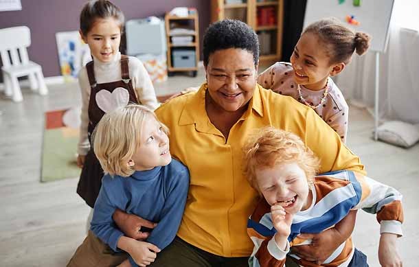 A happy childcare staff member plays with children at their childcare centre