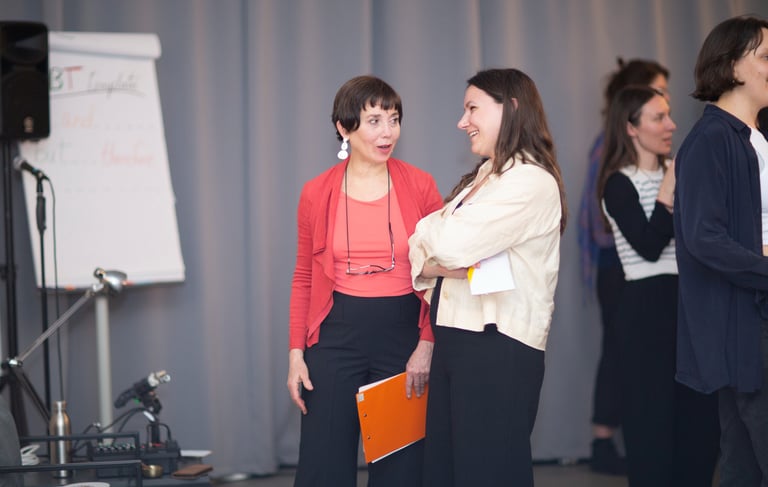 Two women. One public speaking coach, talking with female participant at public speaking workshop. 